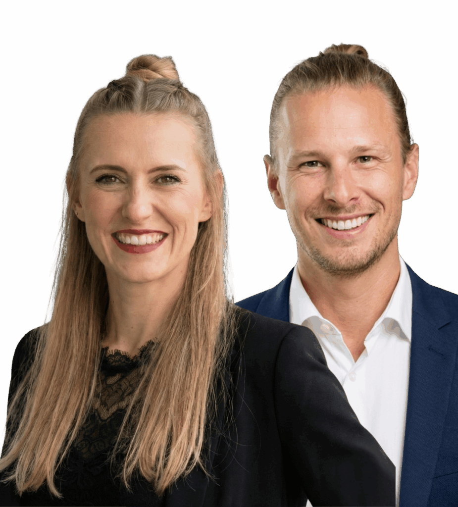 Zwei Personen in Business-Kleidung lächeln in die Kamera. Frau mit blondem Haar und Dutt, schwarzem Oberteil. Mann mit blondem Haar, Bart und dunklem
